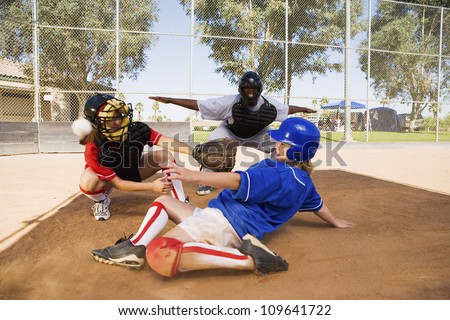 Softball player sliding into base with baseman and umpire