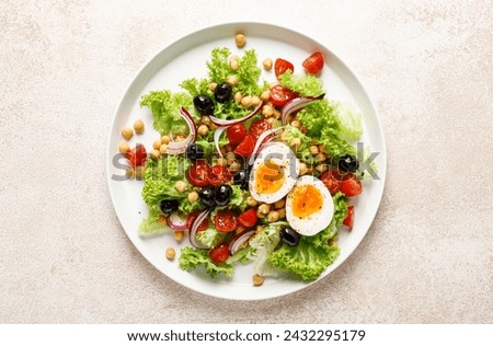 Soft-boiled egg Easter fresh vegetable salad with tomatoes, chickpea, olives, onion and green lettuce. Healthy food,  breakfast. Top view