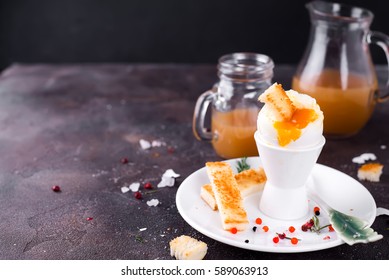 The soft-boiled egg in an eggcup with toasted bread on a dark stone background - Powered by Shutterstock