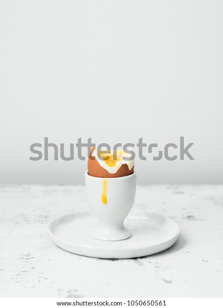 Soft-boiled\
egg in eggcup with yolk on white stone\
table.