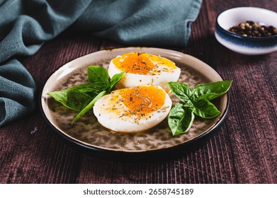 Soft-boiled egg split in half with spices and basil leaves on a plate on a table