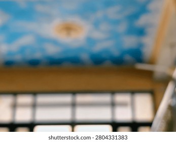 A soft-focus image capturing an interior ceiling adorned with a mural of a blue sky and fluffy white clouds, with a prominent bright light source at its center, creating an ethereal ambiance.