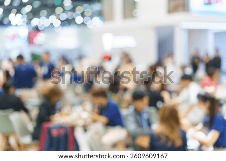 soft-focus scene of bustling attendees sitting and mingling in an exhibition hall, showcasing networking, social gatherings, and a lively atmosphere.