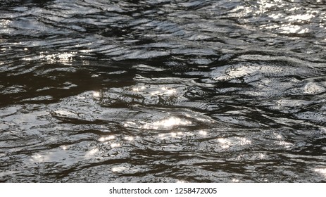 Soft-focused beautiful sun glare glistening and shimmering on the wavy river surface on a sunny day, creating beautiful texture and dynamic patterns