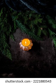 A Softly Light Candle Casting A Warm Glow Against A Dark Background Surrounded With Pine Boughs