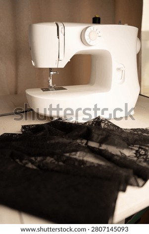 softly lit close-up of a white sewing machine on a wooden tabletop, needle poised above delicate black lace, warm beige backdrop evoking an intimate, modern domestic sewing workspace, crop, depth