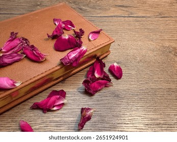 A softly lit composition with a leather notebook with gilded edges, on which half-wilted tea rose petals are scattered. Warm wooden texture creates an atmosphere of coziness and nostalgia.