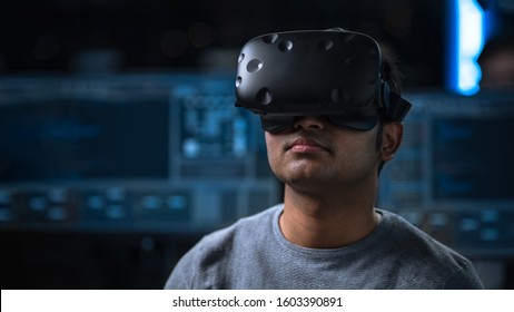 Software Delevoper Wearing Virtual Reality Headset on His Head, Developing and Programming VR Game or Application. In the Background Technology Developing Studio with Computers and Monitors