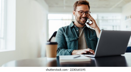 Software designer discussing a new project with his client on the phone. Creative business man working on a laptop in an open plan office. - Shutterstock ID 2230165195