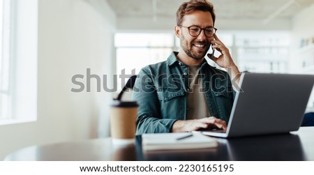 Software designer discussing a new project with his client on the phone. Creative business man working on a laptop in an open plan office.