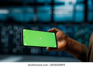 A software developer checks server performance on a mockup smartphone and monitors system alerts through a green screen display.
