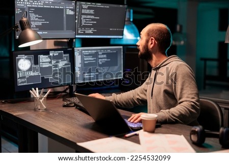Software developer coding database on multiple monitors to program new server interface at night. Workign after hours to develop html source code on terminal window, artificial intelligence.