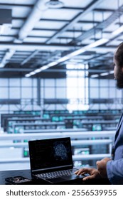 Software developer in data center using laptop to visualize artificial intelligence neural networks made up of interconnected nodes. Server room worker oversees AI systems processing information