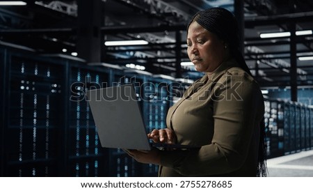Software developer in data center using laptop to upgrade systems for increased stability. Server hub employee configuring equipment rigs with notebook for optimum performance, camera A