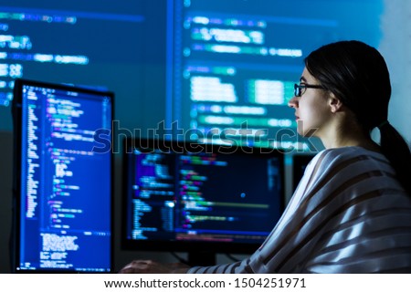 Software developer freelancer woman female in glasses work with program code C++ Java Javascript on wide displays at night Develops new web desktop mobile application or framework Projector background