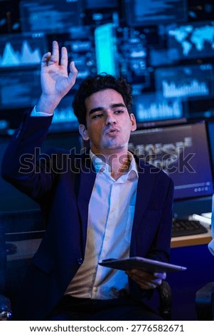 Software developer gesturing to explain complex algorithm logic on a high tech display screen in a modern office at night.