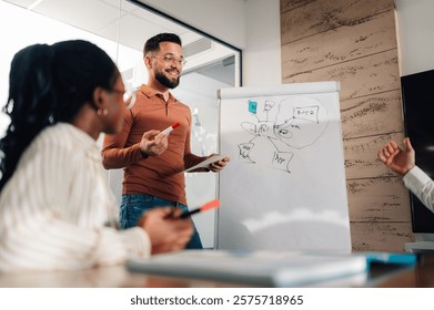 Software developer holding tablet and marker explaining app architecture and pointing at whiteboard to colleagues during a meeting in the office