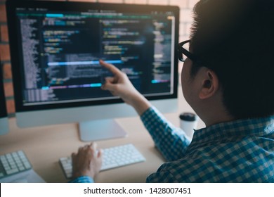 Software developer pointing to the computer screen and is analyzing the code.