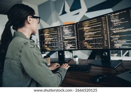 A software developer working diligently on her dual monitor setup, showcasing code and a focused environment in a modern workspace.