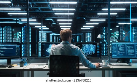 Software Developer Works with AI Analysis on his Computer with Two Monitors. Developer Coding while Looking at the Display of Computer. Modern Evening Dark Office. Back view. - Powered by Shutterstock