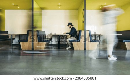 Software developer works on his laptop in a busy coworking office. Surrounded by business people, he focuses on coding in his booth. Vibrant workplace where professionals engage in remote work.