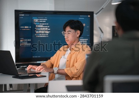Software developer writes code for artificial intelligence on a desktop computer during a collaborative technology project in a contemporary office
