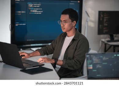 Software developer writing code at a laptop with programming displays in a modern technology workspace