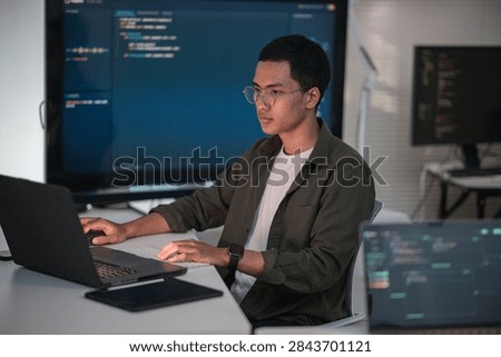 Software developer writing code at a laptop with programming displays in a modern technology workspace