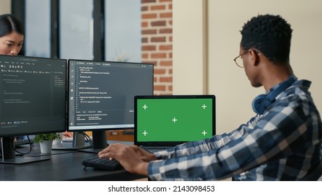 Software Developer Writing Code Using Computer Keyboard And Laptop With Green Screen Chroma Key Mockup Sitting At Desk. Programer Looking At Multiple Screens With Machine Learning Algorithm.