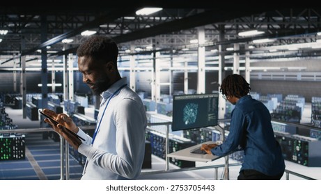 Software developers on data center industrial platform analyzing performance outputs on devices. Server room IT specialists collaborating on finetuning mainframes configurations,