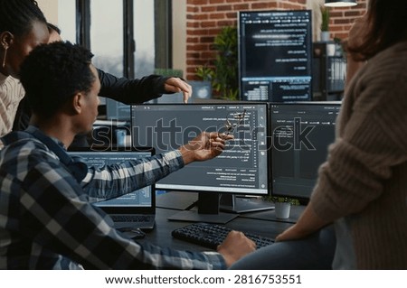 Software developers review source code compiling errors with the team, asking for explanations in front of multiple screens running algorithms.