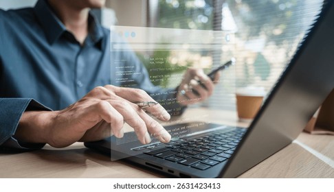 Software development. Programming engineer. Coding application. A man is typing on a laptop with a cell phone in front of him. The laptop screen is displaying a text message.