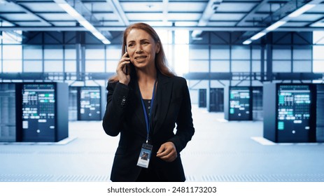 Software engineer talking on smartphone in data center, coordinating server maintenance tasks. Woman surrounded by server racks and high tech equipment, speaking during telephone call, camera B