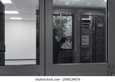 Software Engineer Working on a Laptop Computer in a Modern Server room. Monitoring Room Big Data Scientist in reflection of the entrance door.