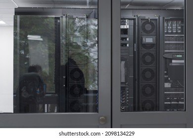 Software Engineer Working on a Laptop Computer in a Modern Server room. Monitoring Room Big Data Scientist in reflection of the entrance door.