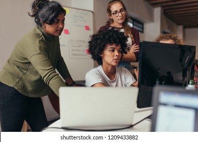 Software engineers working on project and programming in company. Startup business group working as team to find solution to problem. Woman programmer working on computer with colleagues standing by.