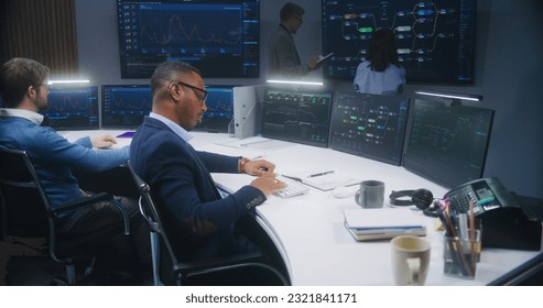 Software programmer sits in front of computer with blockchain network database in monitoring control room. Team of IT technical specialists work with real-time analysis charts on big digital screens. - Shutterstock ID 2321841171