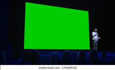 Software Startup Founder Does Presentation Of New Product To The Audience, Behind Him Movie Theater With Green Screen, Mock-up, Chroma Key. Business Conference Live Event Or Device Reveal