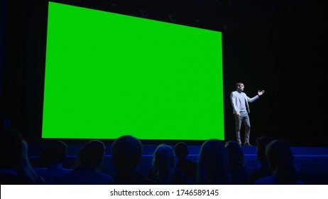 Software Startup Founder Does Presentation Of New Product To The Audience, Behind Him Movie Theater With Green Screen, Mock-up, Chroma Key. Business Conference Live Event Or Device Reveal