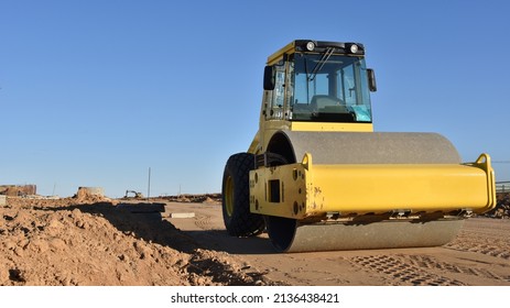 Soil Compactor leveling ground at construction site. Vibration single-cylinder road roller on construction road. Road work and asphalt laying. Tower cranes build high-rise buildings. Road construction - Powered by Shutterstock