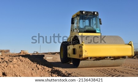 Soil Compactor leveling ground at construction site. Vibration single-cylinder road roller on construction road. Road work and asphalt laying. Tower cranes build high-rise buildings. Road construction