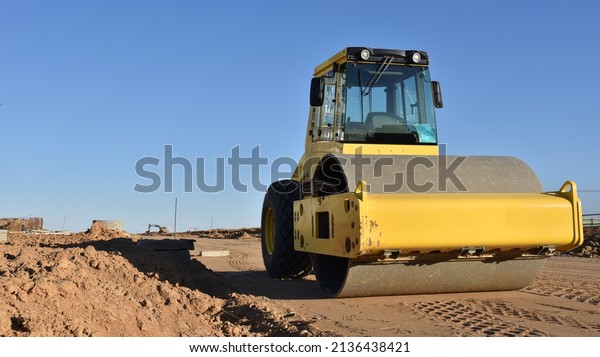 Soil Compactor leveling ground at\
construction site. Vibration single-cylinder road roller on\
construction road. Road work and asphalt laying. Tower cranes build\
high-rise buildings. Road\
construction