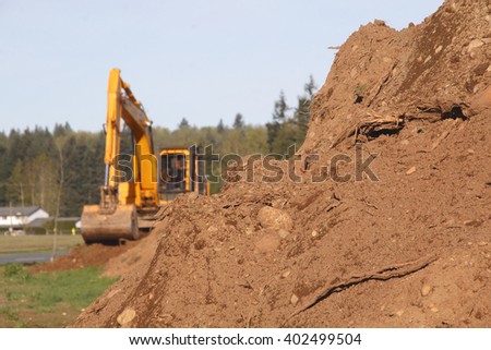 Soil or dirt in the foreground with an industrial shovel in the background/Heavy Lifters and Moving Earth/An industrial shovel a pile of dirt. 