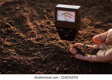 A soil meter and a farmer's hands are picking up soil for planting. - Shutterstock ID 2160763753