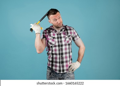 A Soiled Hard Worker With Gloves And A Tattered Shirt Scratches His Head With The Handle Of A Hammer, Reflecting On Something. Isolated On Blue