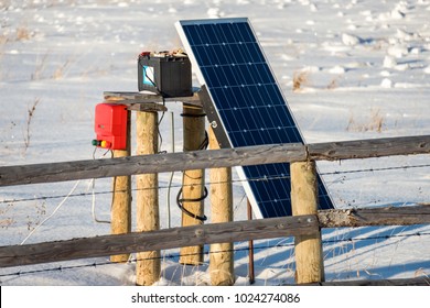 The Solar Battery Charges The Device For Electric Fencing Of Haystacks From Wild Animals In The Snowy, Winter Field Of An Agricultural Farm