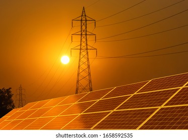 Solar Cells Or Photovoltaics In Solar Power Plant With  Silhouette High Voltage Electric Pylon Pillar Substation  On Sunset   