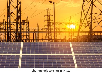 Solar Cells In Power Station With High Voltage Electric Pillars Substation On Sunset