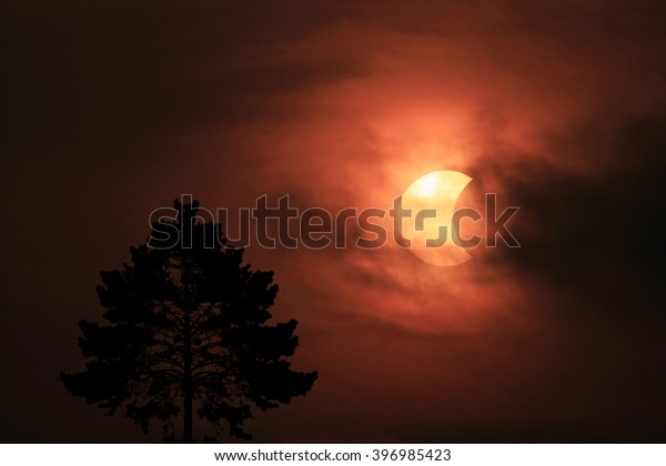 Solar eclipse with clouds and silhouettes\
foreground image.