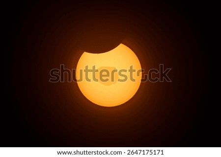 Solar eclipse nearly over with only a small part of the sun oscurred by the moon, sunpots visible on the sun's surface